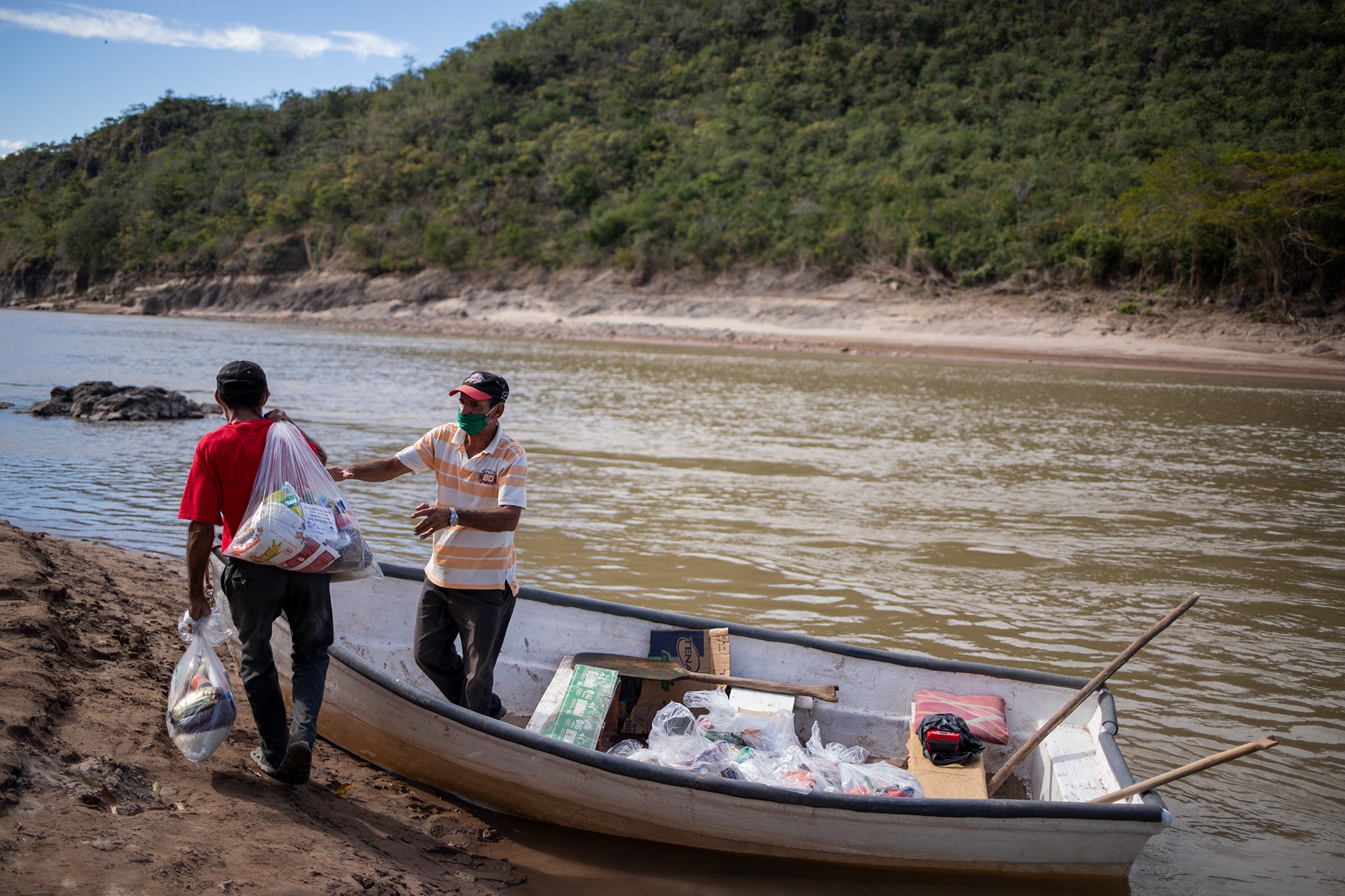 Visitación Paz Muñoz, de 65 años y camiseta a rayas, conduce la lancha del Patronato de la comunidad de La Isla Colina, para ayudar a que sus vecinos logren cruzar de un lado a otro el río Ulúa. Santa Bárbara, 25 de enero de 2021. Foto: Martín Cálix.