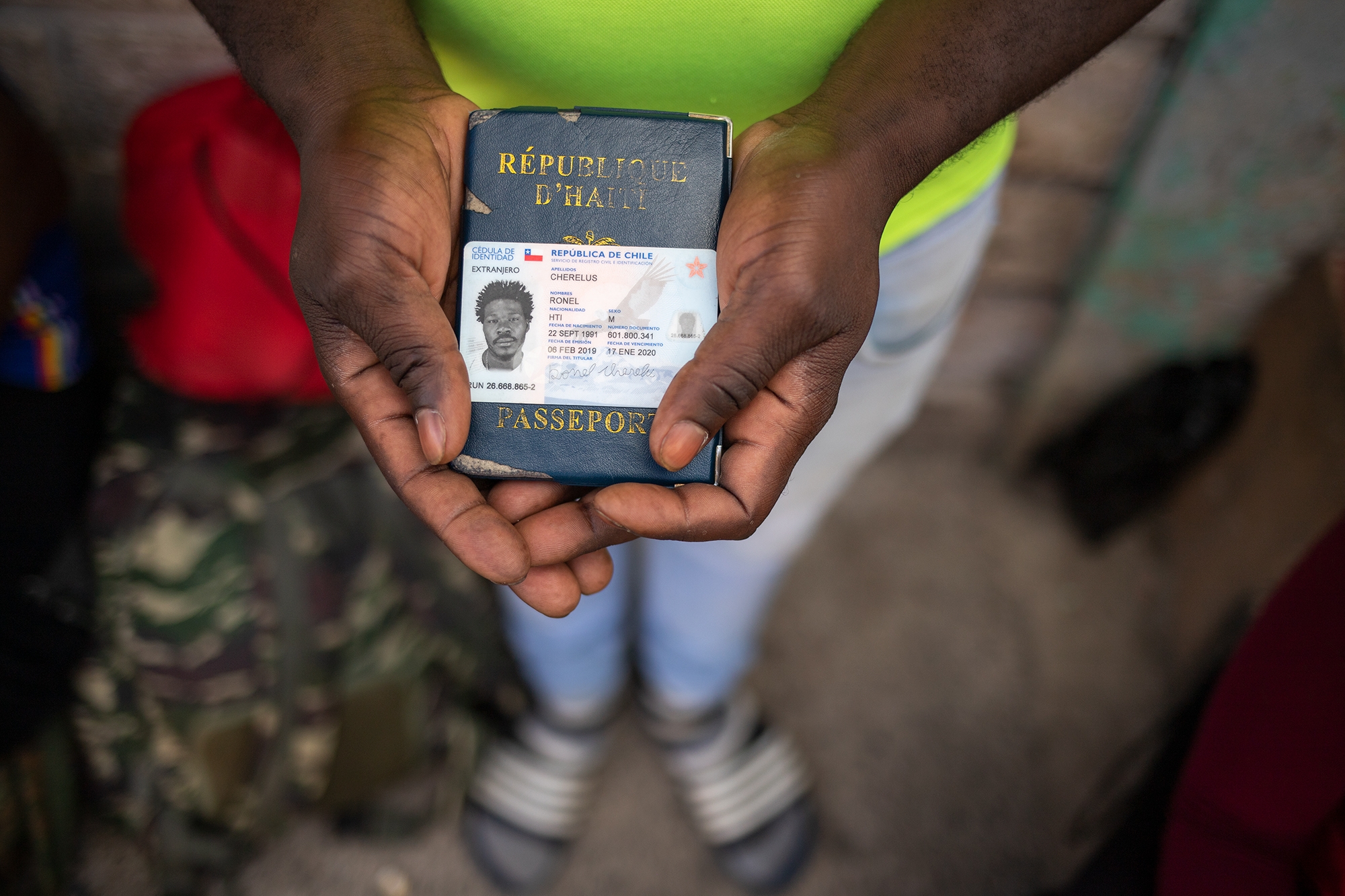 Ronel sostiene sus documentos de identificación en sus manos, sobre su pasaporte haitiano, el documento de residencia chileno vencido desde el 17 de enero de 2020. El Gobierno chileno no renovó su solicitud de residencia. Comayagüela, 26 de octubre de 2021. Foto: Martín Cálix.