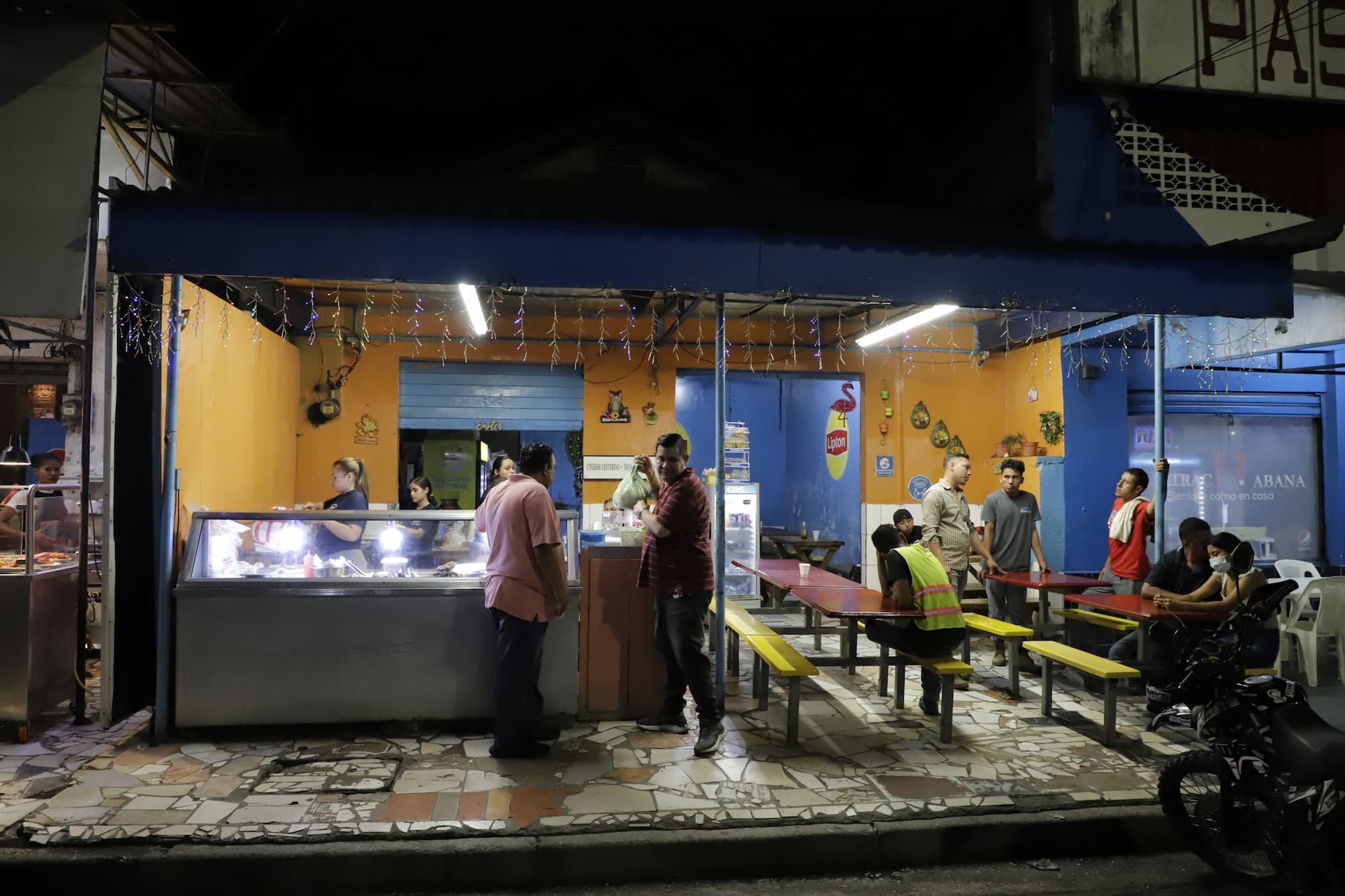 Ante el toque de queda ordenado por la presidenta Xiomara, algunos empleados que trabajan en los puestos de venta de baleadas en la tercera avenida del centro de San Pedro Sula, deben dormir en colchones de forma improvisada en sus negocios. Fotos CC/Amílcar Izaguirre.