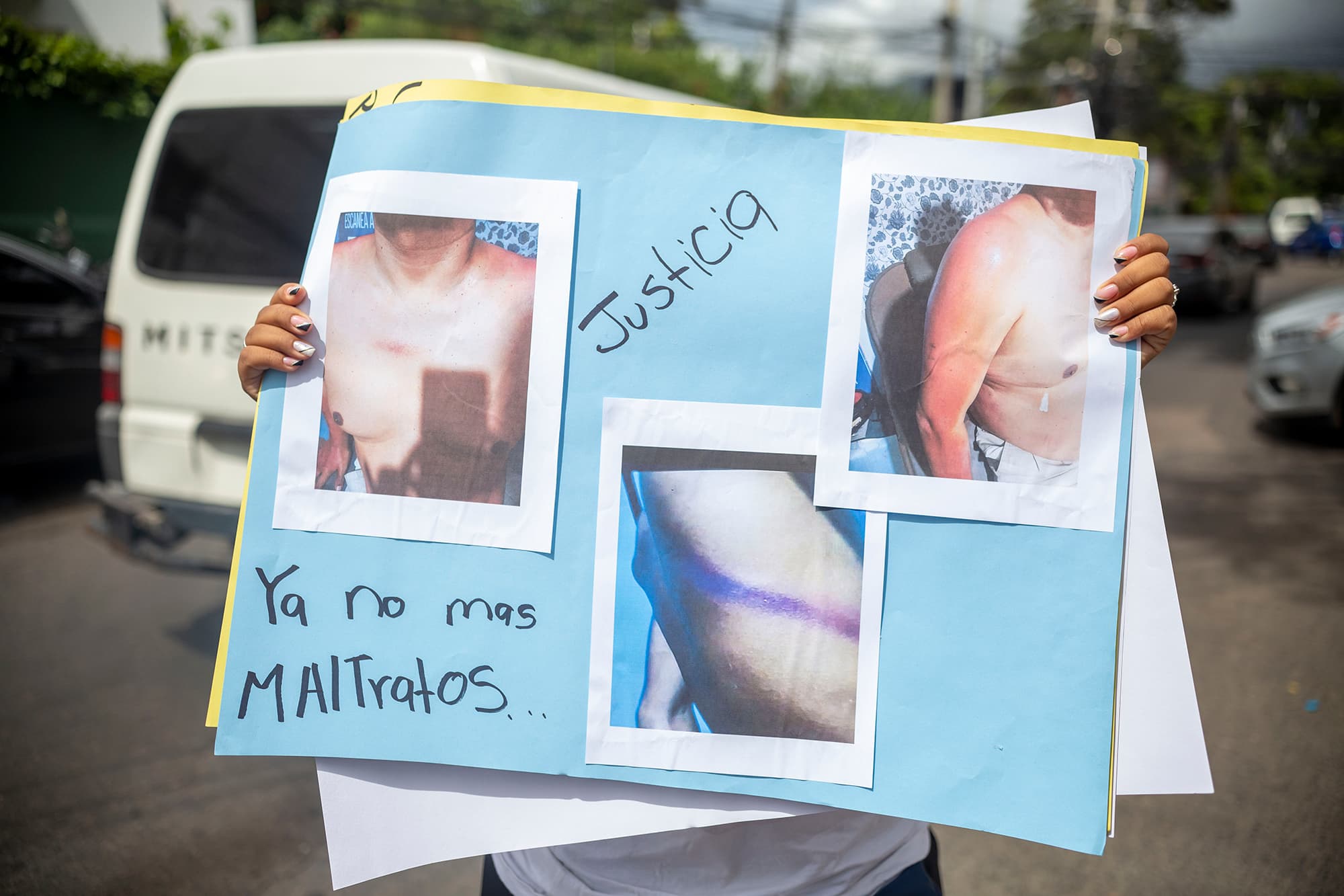 Un familiar de un privado de libertad levanta una pancarta con las fotos de los maltratos que han sufrido sus parientes en la cárceles bajo el control de la PMOP. Foto CC/Fernando Destephen