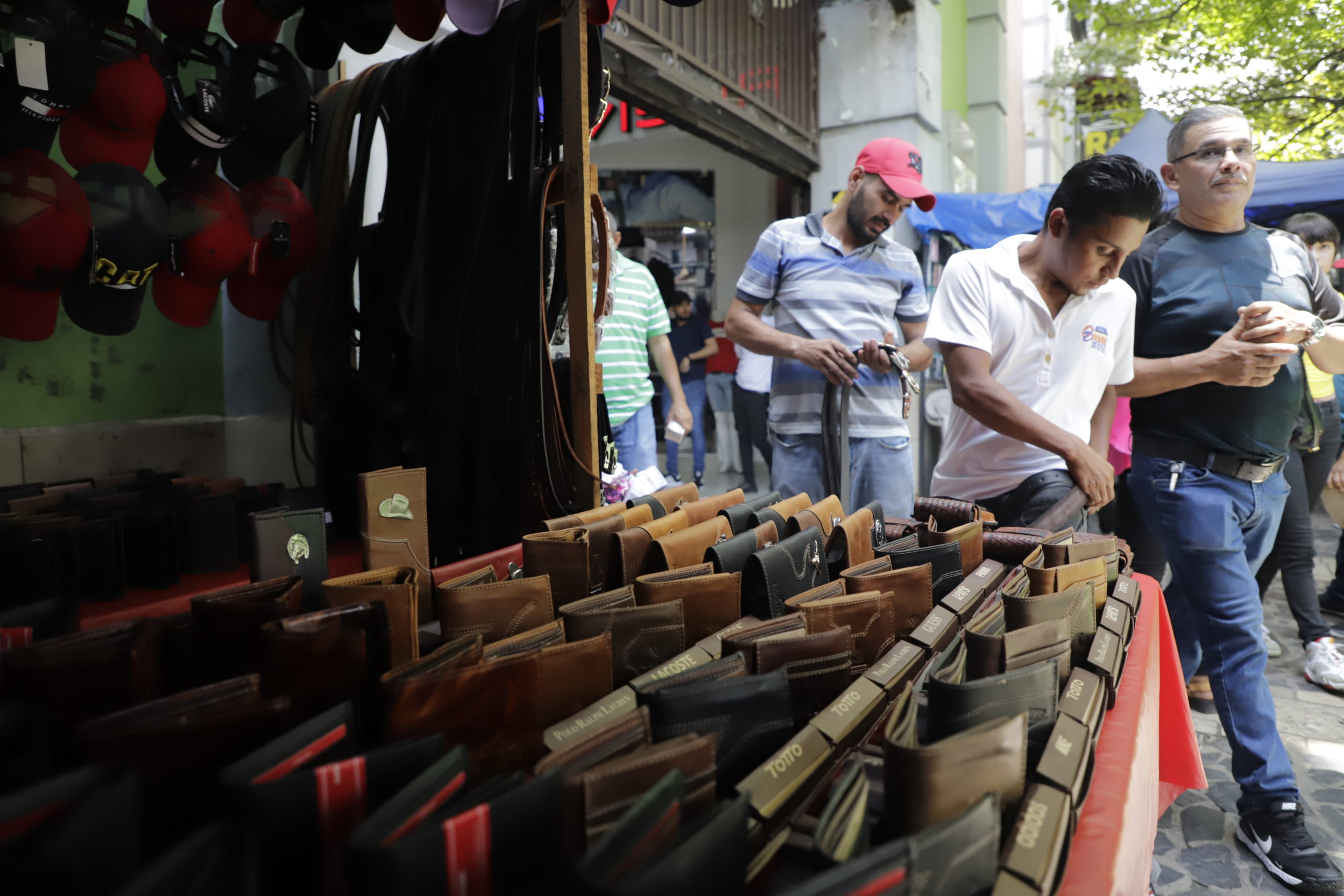 Un joven se talla una faja en el  puesto de venta informal mientras los transeúntes caminan por la zona peatonal de la segunda calle en San Pedro Sula. Foto CC/Amilcar Izaguirre