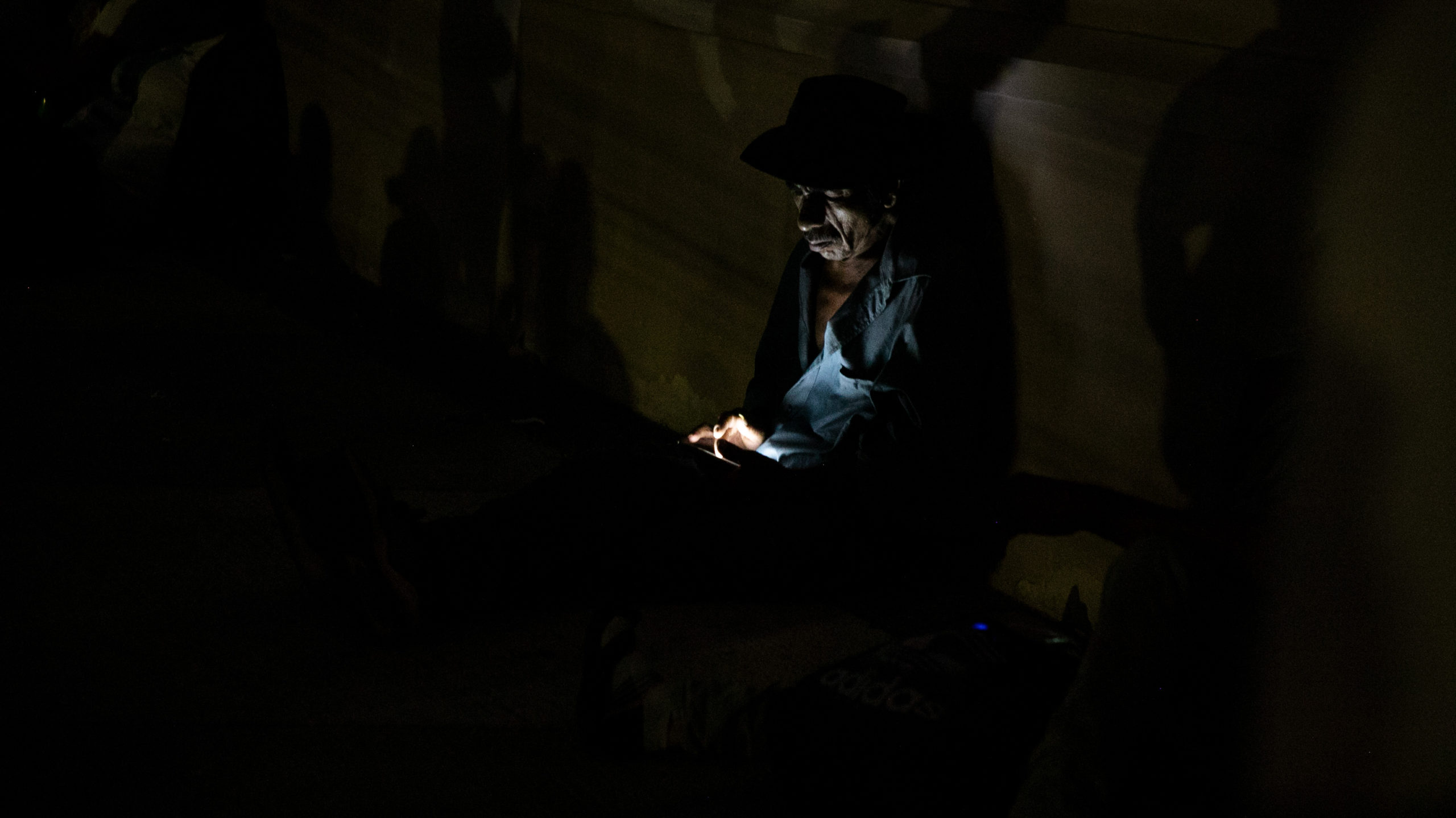 Durante la jornada de movilización a Tegucigalpa, un campesino revisa su teléfono celular recostado en la pared frontal del paraninfo de la Universidad Nacional Autónoma de Honduras (UNAH). Tegucigalpa, septiembre de 2024. Foto CC / Fernando Destephen.