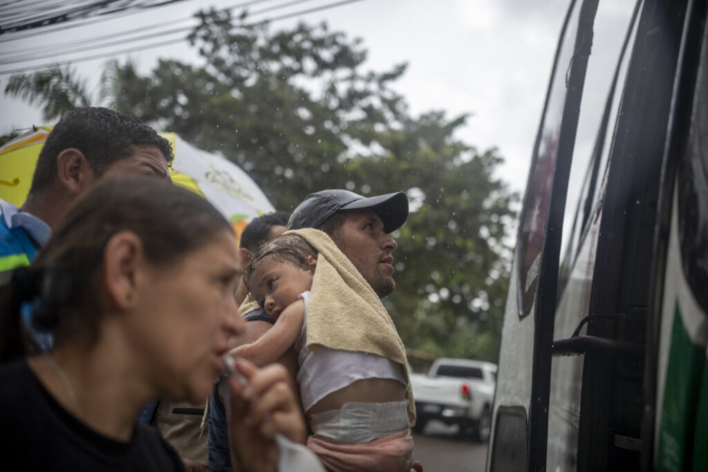 2023-08-24Danlí-MigrantesVenezolanos-Buses11 - Contra Corriente Un hombre venezolano en tránsito migratorio carga a su hijo mientras aborda un bus gratuito que los trasladará hasta la frontera con Guatemala. Danlí, El Paraíso, 24 de agosto de 2023. Foto CC / Fernando Destephen.