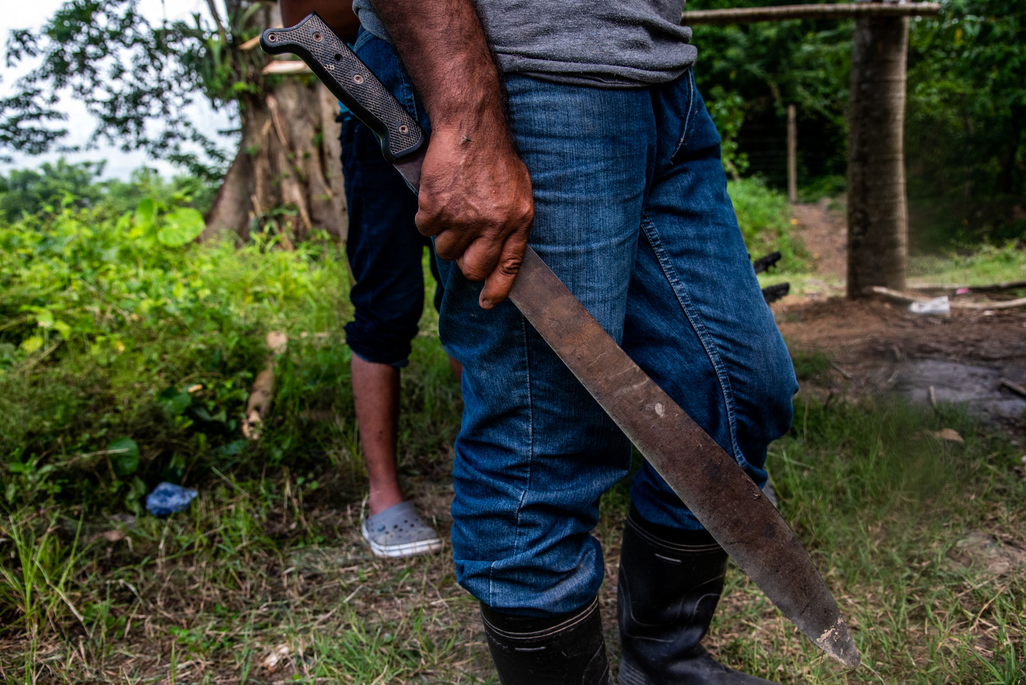 A la izquierda, un campesino carga un machete, herramienta de trabajo en las plantaciones y  símbolo de la lucha por las tierras. A la derecha, imagen drone del río Aguán desde la cooperativa Tranvío, atacada por un comando armado en enero de 2025. Fotos de Seth Berry.